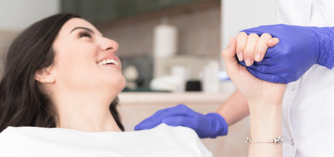 young woman smiling calmly shaking hands with dentist in blue gloves
